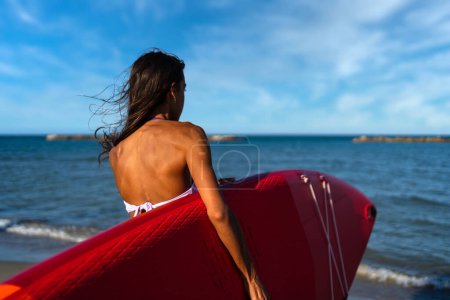 Foto de Mujer joven sosteniendo Stand Up Paddle Board, SUP, en un día soleado en verano. Concepto de vida activa. - Imagen libre de derechos
