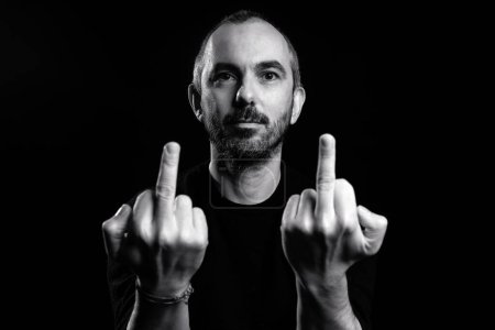 Photo for Middle age man against black background showing middle finger in a provocative way. Black and white image. Concept of hate, aggressive behaviour. - Royalty Free Image