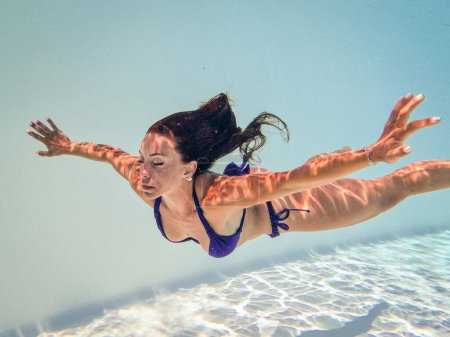 Photo for Underwater woman portrait with blue bikini spreading arms with closed eyes inside swimming pool. Relaxing in summer time. - Royalty Free Image