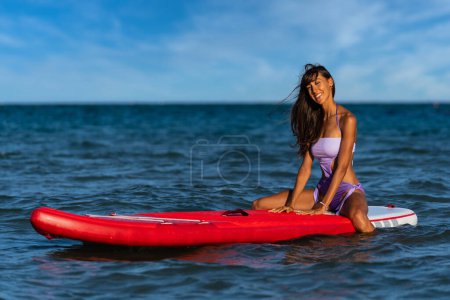 Téléchargez les photos : Jeune belle femme souriante portrait sur Stand Up Paddle Board, SUP, par une journée ensoleillée en été. Concept de vie active. - en image libre de droit