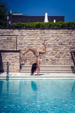 Téléchargez les photos : Jeune femme en forme à l'envers faisant le handstand dans une piscine. Image filtrée. - en image libre de droit