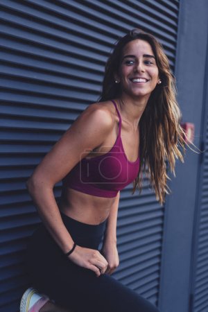 Foto de Joven mujer atlética caucásica sonriente retrato al aire libre contra la pared oscura. Estilo de vida activo. - Imagen libre de derechos