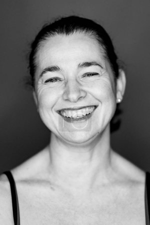 Téléchargez les photos : Portrait souriant de tête de studio de femme d'âge moyen sur fond sombre. Image en noir et blanc. - en image libre de droit