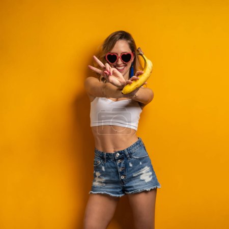 Foto de Retrato de mujer sosteniendo plátano divirtiéndose contra fondo naranja colorido. Concéntrate en las manos. - Imagen libre de derechos