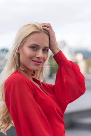 Photo for Smiling blonde woman close up portrait wearing red dress outdoors. - Royalty Free Image