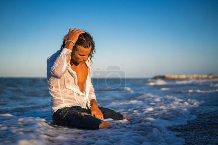 Photo for Youn fit sexy man portrait on the beach at sunset wearing jeans and shirt. - Royalty Free Image