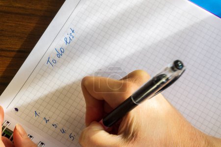 Foto de Primer plano de las manos de la mujer escribiendo en cuaderno en espiral colocado en el escritorio de madera. Para hacer la lista - Imagen libre de derechos