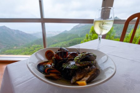 Photo for Tasty mussels on a table with a glass of a fine white wine. Beautiful view with mountains on the background. - Royalty Free Image