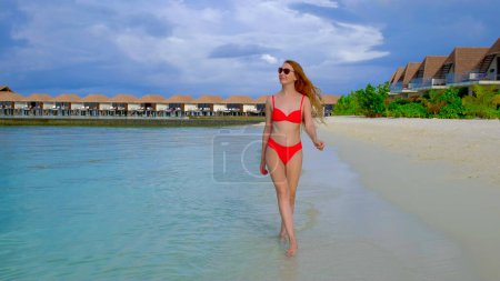 Foto de Una mujer en bikini está caminando. La hembra es feliz en Maldivas. Océano azul turquesa en el fondo. Chica disfruta de sus vacaciones tropicales. Concepto de vacaciones de verano. - Imagen libre de derechos