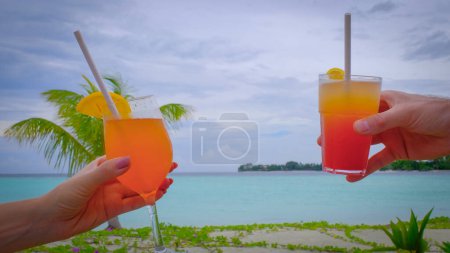 Photo for Close up of hands with cocktails making a toast. Romantic couple are clinking with glasses.Blue turquoise ocean on the background. Couple enjoys her tropical holidays. Summer travel vacation concept. - Royalty Free Image