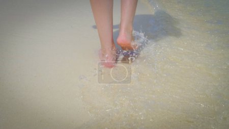 Téléchargez les photos : Gros plan d'une femme marchant sur une plage de sable blanc exotique aux Maldives. Des éclaboussures et des vagues d'eau claire. Voyage d'été concept de vacances. - en image libre de droit