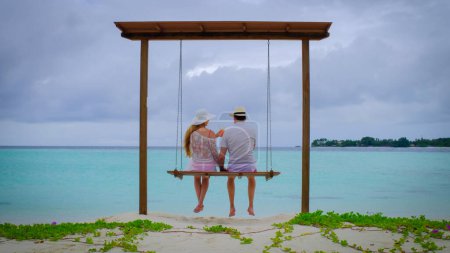 Foto de Un par está en columpios. El hombre y la mujer son felices en Maldivas. Océano azul turquesa en el fondo. Chica disfruta de sus vacaciones tropicales. Concepto de vacaciones de verano. - Imagen libre de derechos