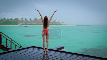 Téléchargez les photos : Une femme en bikini est heureuse aux Maldives sous la pluie. Pluie abondante. Océan bleu turquoise sur le fond. Fille profite de ses vacances tropicales. Voyage d'été concept de vacances. - en image libre de droit