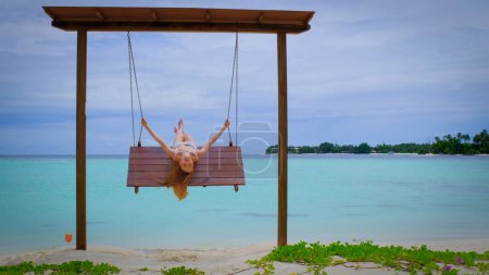 Téléchargez les photos : La femme en bikini est sur les balançoires. Femelle est heureuse aux Maldives. Océan bleu turquoise sur le fond. Fille profite de ses vacances tropicales. Voyage d'été concept de vacances. - en image libre de droit