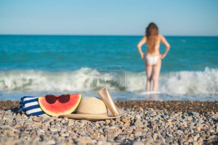 Foto de Hat, a towel and sunglasses. Tall woman with a long hair from a back is on a beach. Mediterranean sea with waves on the background. Blue and turquoise water. Vacation summer vibe. Slow motion video. - Imagen libre de derechos