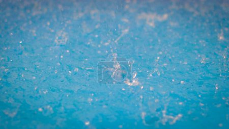 Téléchargez les photos : Gouttelettes congelées. Gros plan d'une goutte. Pluie sur une surface d'eau de piscine bleue. Grandes éclaboussures de grêle tombant. - en image libre de droit