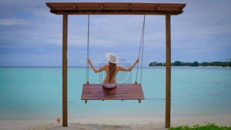 Foto de La mujer en bikini está en columpios. La hembra es feliz en Maldivas. Océano azul turquesa en el fondo. Chica disfruta de sus vacaciones tropicales. Concepto de vacaciones de verano. - Imagen libre de derechos