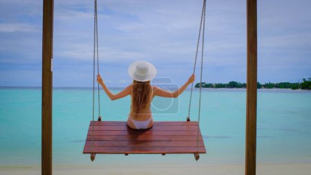 Foto de La mujer en bikini está en columpios. La hembra es feliz en Maldivas. Océano azul turquesa en el fondo. Chica disfruta de sus vacaciones tropicales. Concepto de vacaciones de verano. - Imagen libre de derechos