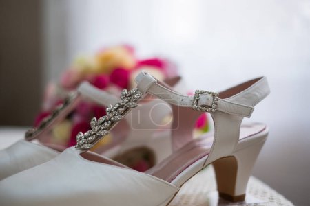 Téléchargez les photos : Close up of wedding shoes. White beautiful shoes of a bride. Flowers on the background. - en image libre de droit