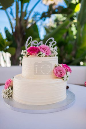 Téléchargez les photos : Gâteau de mariage décoré de fleurs roses. Image pour un menu ou un catalogue de confiseries. Gros plan d'un gâteau blanc avec des lettres d'amour. Photo de haute qualité. - en image libre de droit