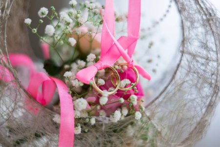Foto de Dos anillos de boda en una cesta. El primer plano de las flores y los anillos de matrimonio con la cinta rosada. Foto de alta calidad. - Imagen libre de derechos