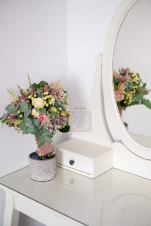 Téléchargez les photos : Boudoir white table with a beautiful bouquet of flowers. Details of the interior of the bedroom for girls and make-up, hairstyles with a mirror. Room decor. - en image libre de droit