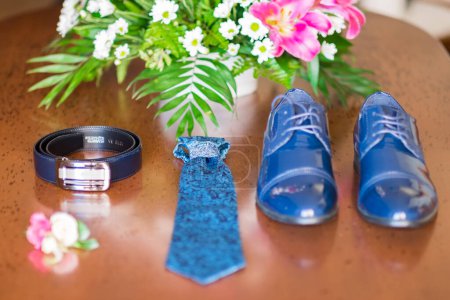 Téléchargez les photos : Close up of small bouquet with flowers laying near man wedding clothes. Close-up of a grooms shoes and a tie. Blue beautiful wedding accessory. - en image libre de droit