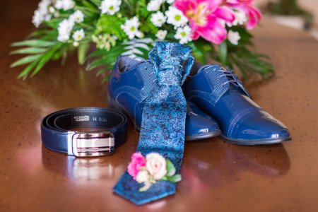 Photo for Close up of small bouquet with flowers laying near man wedding clothes. Close-up of a grooms shoes and a tie. Blue beautiful wedding accessory. - Royalty Free Image