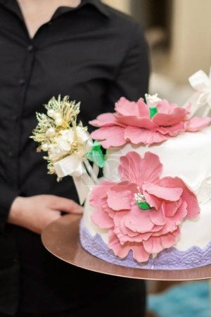 Téléchargez les photos : Wedding cake decorated with pink flowers. Picture for a menu or a confectionery catalog. Close up of a white cake with a woman. Girl holding a cake. High quality photo. - en image libre de droit
