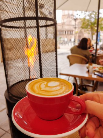 Foto de Una taza de café en la mesa. Cerrar taza de café blanco con forma de corazón de latte art foam. Taza roja. Foto vertical. - Imagen libre de derechos