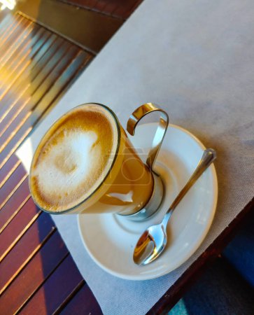 Foto de Una taza de café en la mesa. Cerrar taza de café blanco con una espuma de arte latte. Foto vertical. - Imagen libre de derechos