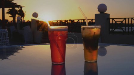 Foto de Dos cócteles en la playa al atardecer. Dos cócteles están sobre una mesa de cristal. Hermosa reflexión sobre un vaso. - Imagen libre de derechos