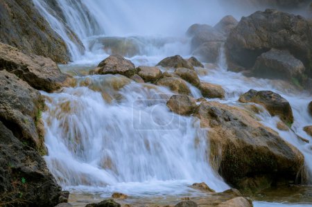 Photo for The image captures a close-up of water flowing over large rocks, creating a series of small cascades and gentle rapids. Mist rises from the water, adding a serene and ethereal atmosphere to the scene. - Royalty Free Image