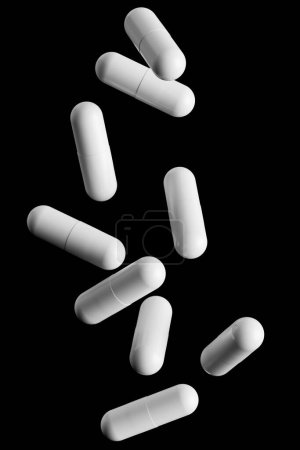 Téléchargez les photos : Pilules blanches tombantes isolées sur fond noir. Maquette ou modèle. 3d rendu - en image libre de droit