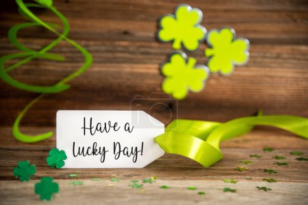 Foto de White Label With English Text Have A Lucky Day Saint Patricks Day Decoration With Green Clover And Shamrock. Wooden Vintage Background With Festive Ribbon. - Imagen libre de derechos
