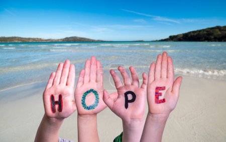 Kinderhände bauen buntes englisches Wort Hope. Sommer Ozean, Meer und Strand als Hintergrund.