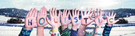 Foto de Children Hands Building Colorful English Word Holistic (en inglés). Fondo blanco de invierno con copos de nieve y paisaje nevado. - Imagen libre de derechos