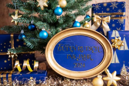 Foto de Marco de oro con texto alemán Guten Rutsch Ins Jahr 2024, significa feliz año nuevo 2024 en inglés, oro, decoración azul de Navidad, árbol de Navidad, fondo de invierno - Imagen libre de derechos