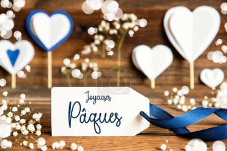 Etikett mit französischem Text Joyeuses Paques bedeutet frohe Ostern. Weiße festliche und stimmungsvolle Dekoration wie Herzen, Blumen und eine blaue Schleife. Vintage, Holz Hintergrund.
