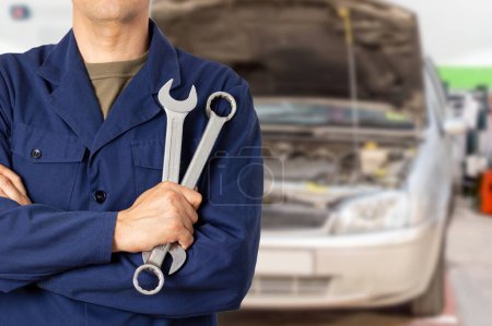 Photo pour Homme mécanicien debout tout en tenant deux clés dans un atelier de mécanique automobile - image libre de droit