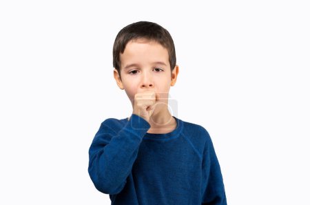 Foto de Niño pequeño con camisa azul sobre un fondo aislado sintiéndose mal y tosiendo como síntoma de resfriado o bronquitis. Concepto de salud. - Imagen libre de derechos