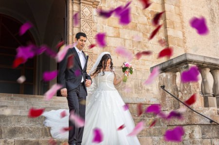 Foto de Shot of a happy newlywed young couple getting showered with rose petals outdoors on their wedding day - Imagen libre de derechos