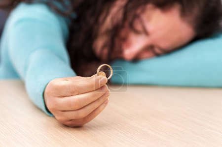 Photo for Closeup of a single sad wife after divorce lamenting holding the wedding ring in a house interior - Royalty Free Image