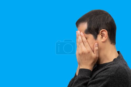 Téléchargez les photos : Close-up view of a man covering his face and crying with blue background - en image libre de droit
