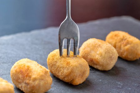 Photo for Close up of picking up homemade croquette with a fork, a typical Spanish black slate dish. - Royalty Free Image