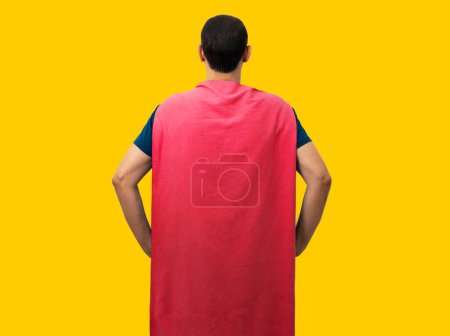 Foto de Young man in superhero costume posing from back against yellow background. - Imagen libre de derechos