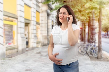 Photo for Shot of a painful pregnant woman calling medical assistance in the city - Royalty Free Image