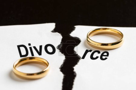 Closeup of a breakup document with the word divorce and two wedding rings on a black table
