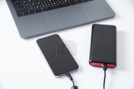 Téléchargez les photos : USB charger plugged in to smart phone with power bank, mobile phone battery on desk at office. - en image libre de droit