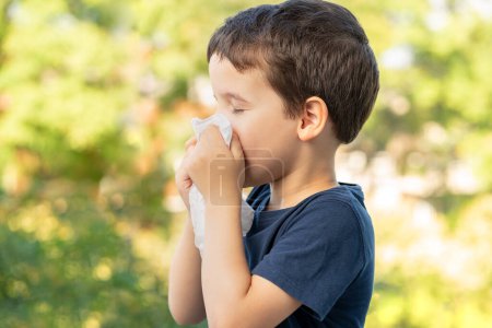 Téléchargez les photos : Allergic child sneezing covering nose with wipe in a park in spring or summer season - en image libre de droit